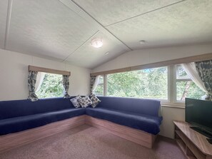 A room with a blue sofa, a television on a wooden stand, and windows with curtains. - 2 bedroom accommodation in Hevingham (Hevingham)