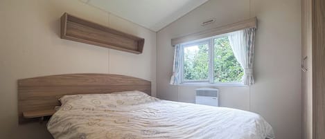 A bedroom with a wooden headboard, a window with curtains, a radiator, and a patterned bedspread.