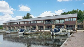 A marina with boats docked in front of a two-story building with large windows and a flat roof. - 1 bedroom accommodation in Carnforth (Carnforth)
