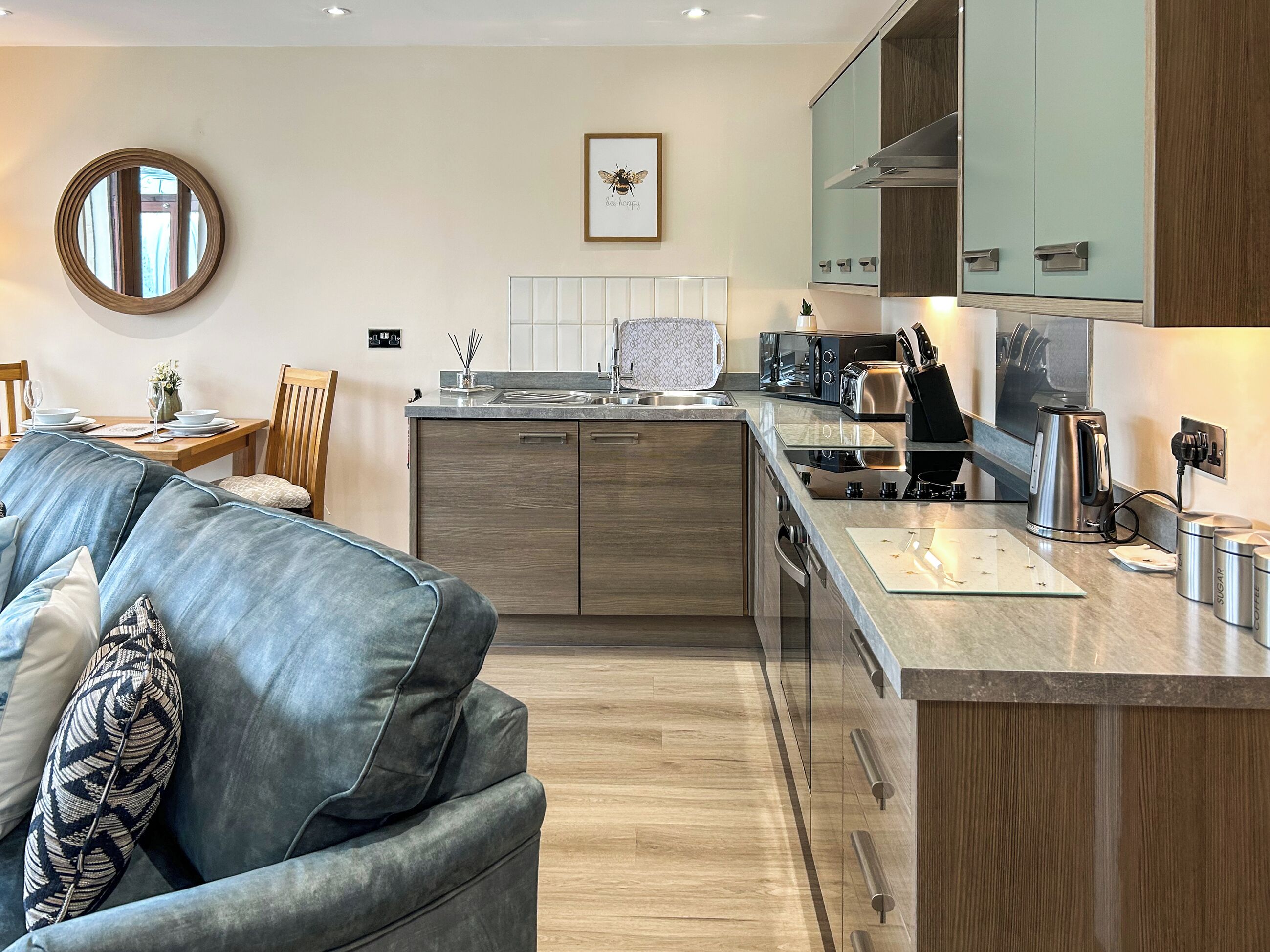 A modern kitchen with a central island, wooden cabinets, and a dining area with a sofa and chairs.