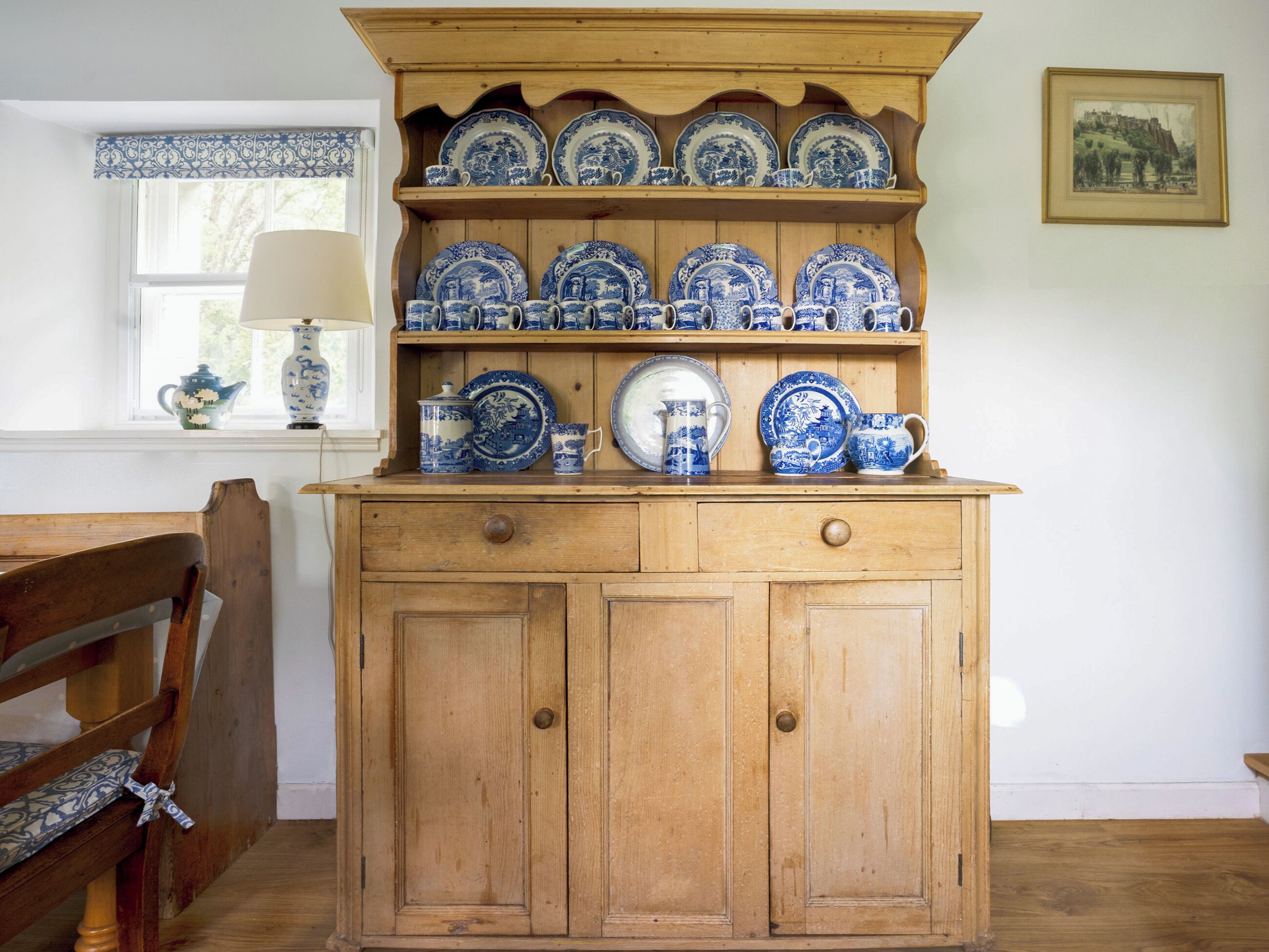 A wooden cabinet with blue and white ceramic dishes and a framed picture on the wall.