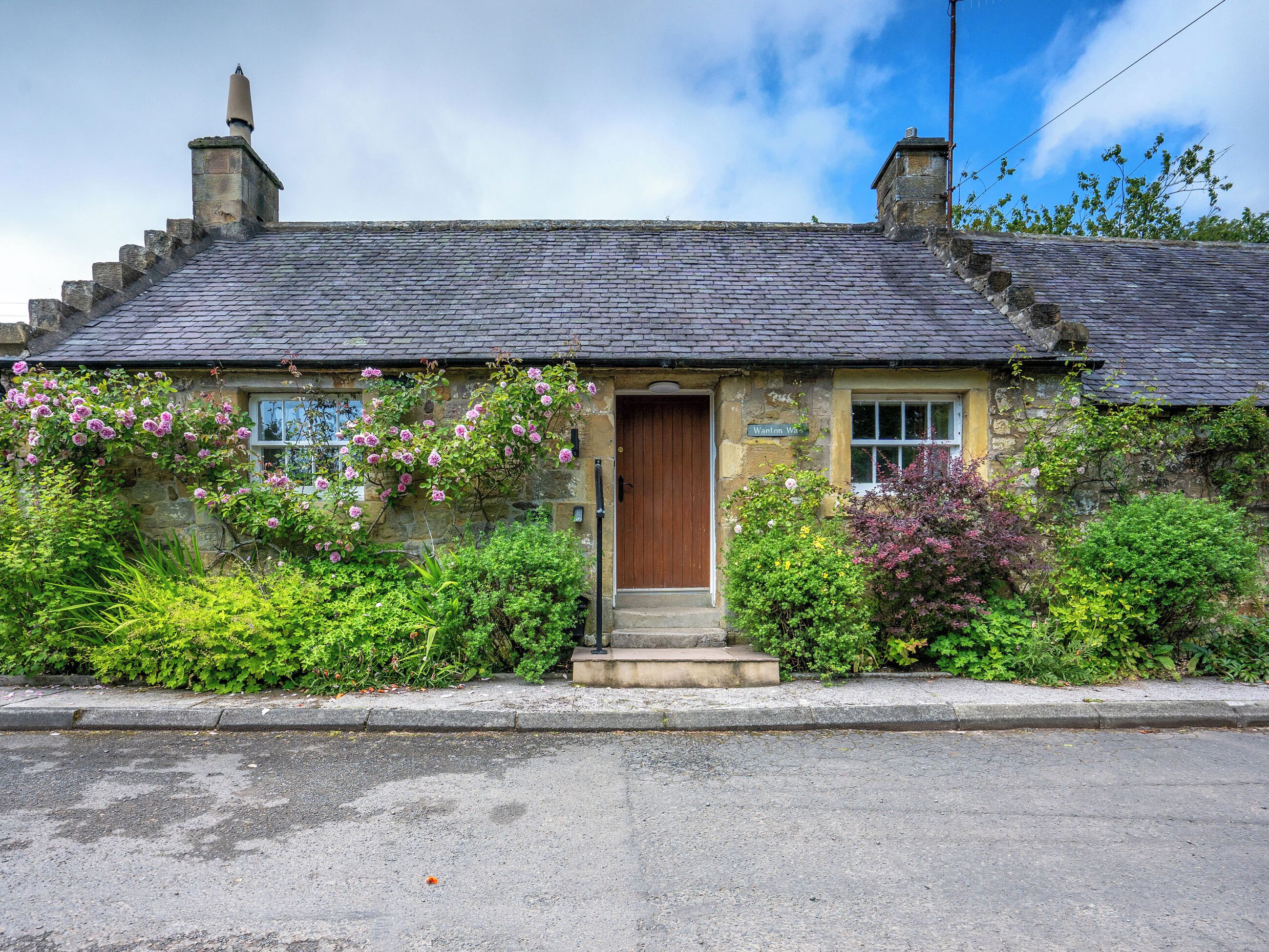 A stone cottage with a wooden door, a chimney, and a sign reading 'Wanton Wa.'