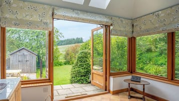 A room with large windows, a wooden table, and a view of a green landscape.