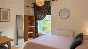 A bedroom with a bed, a desk, a mirror, and a window with curtains. - 2 bedroom accommodation in Norwich (Norwich)