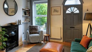 A living room with a fireplace, a striped armchair, a green sofa, and a brown ottoman. - 2 bedroom accommodation in Norwich (Norwich)