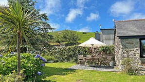 A stone building with a patio, outdoor seating, and a view of a green hillside. - Mum's Cottage - UK52136 (Minions)