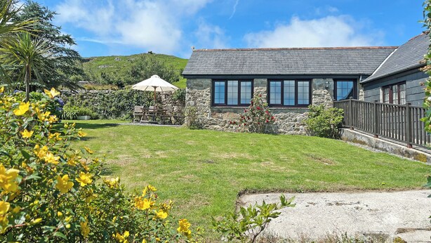 A stone house with a grassy yard, a wooden deck, and a mountain in the background. - Mum's Cottage - UK52136 (Minions)