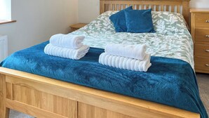Ein Bett mit blauer Bettdecke, zwei Kissen und zwei gefaltete Handtücher.