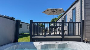 A hot tub with a wooden deck and an umbrella, a house with a window, and a clear blue sky. - Victory Wisteria Lodge (Patrington Haven)