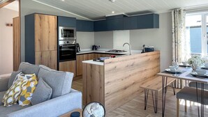 A modern kitchen with a central island, a dining area with a table set for two, and a living area with a sofa and a globe. - Victory Wisteria Lodge (Patrington Haven)