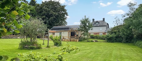 Ein Haus mit Garten, einer Holzterrasse und einem großen Baum im Hintergrund.