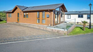 Un edificio de madera con techo inclinado, ventanas amplias y entrada pavimentada.