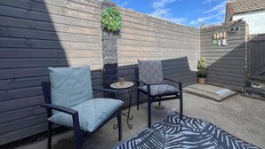 Une terrasse avec deux chaises et une table, un pilier en pierre orné de verdure et une clôture en bois.