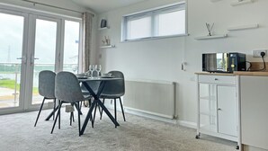 A modern kitchen with a microwave, white cabinetry, and a dining area with a table and chairs. - The Estuary Lodge - UK52152 (Staynall, near Poulton-le-Fylde)