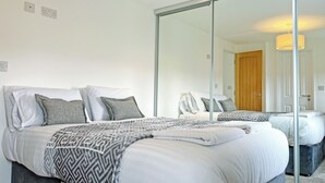 A bedroom with a large mirror, a bed with patterned bedding, a wardrobe, and a door. - The Estuary Lodge - UK52152 (Staynall, near Poulton-le-Fylde)