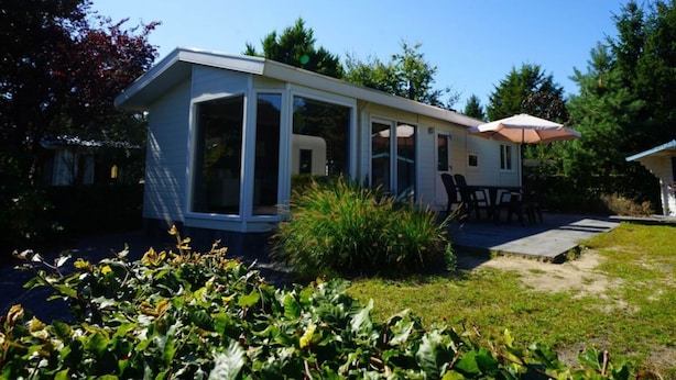 Einbungalow mit überdachter Terrasse, einer kleinen Holzterrasse und einem Garten mit verschiedenen Pflanzen.
