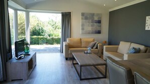 Ein modernes Wohnzimmer mit zwei Sofas, einem Couchtisch, einem Fernseher auf einem Schrank und einem großen Fenster mit Vorhängen.