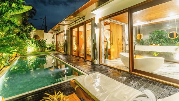 Un hotel moderno con piscina infinita, terraza de madera y una amplia bañera interior.