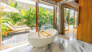 Un baño moderno con una bañera independiente, cubierta de madera y exuberante vegetación tropical.