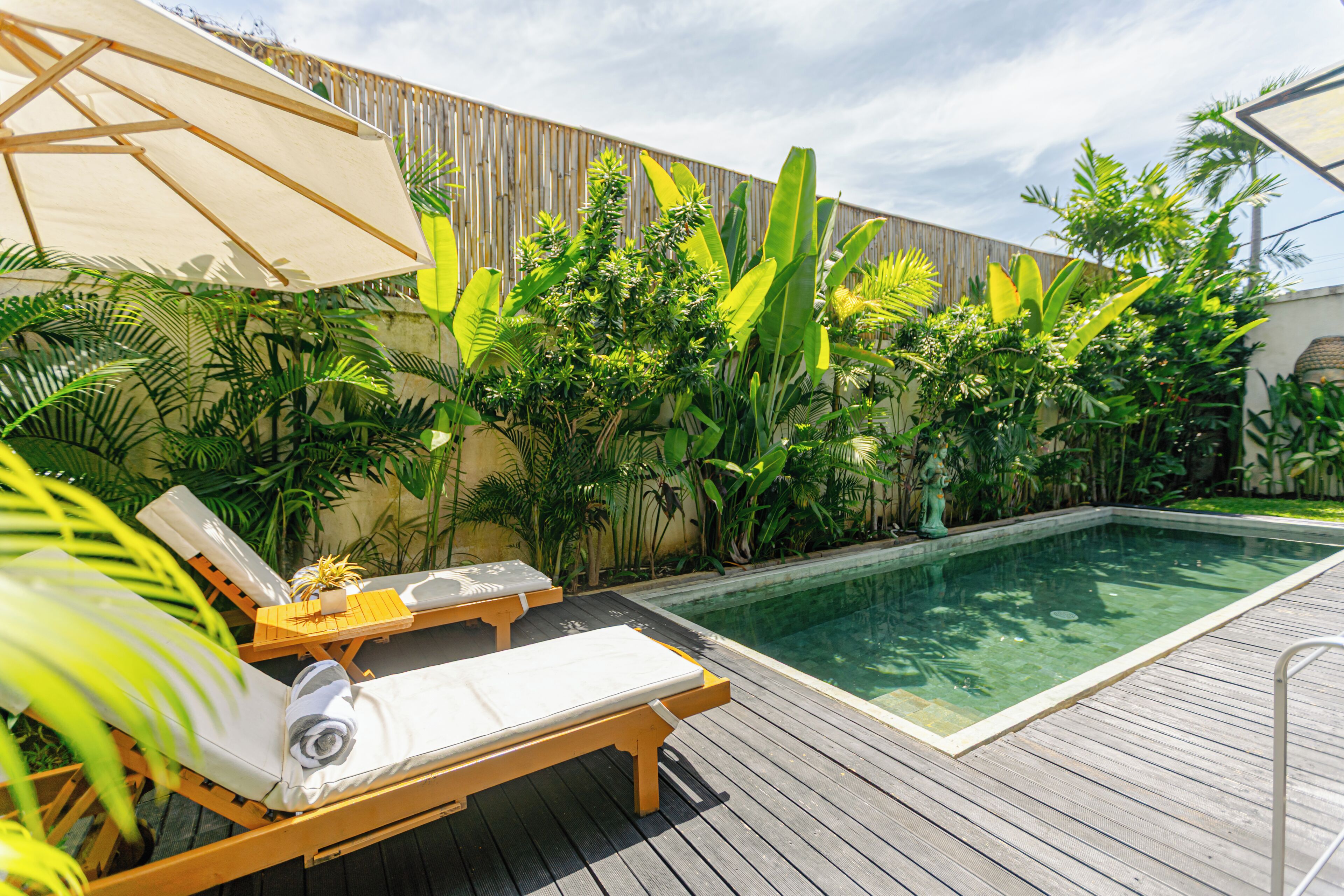 Zona de piscina con terraza de madera, sillas de descanso y diversas plantas tropicales.