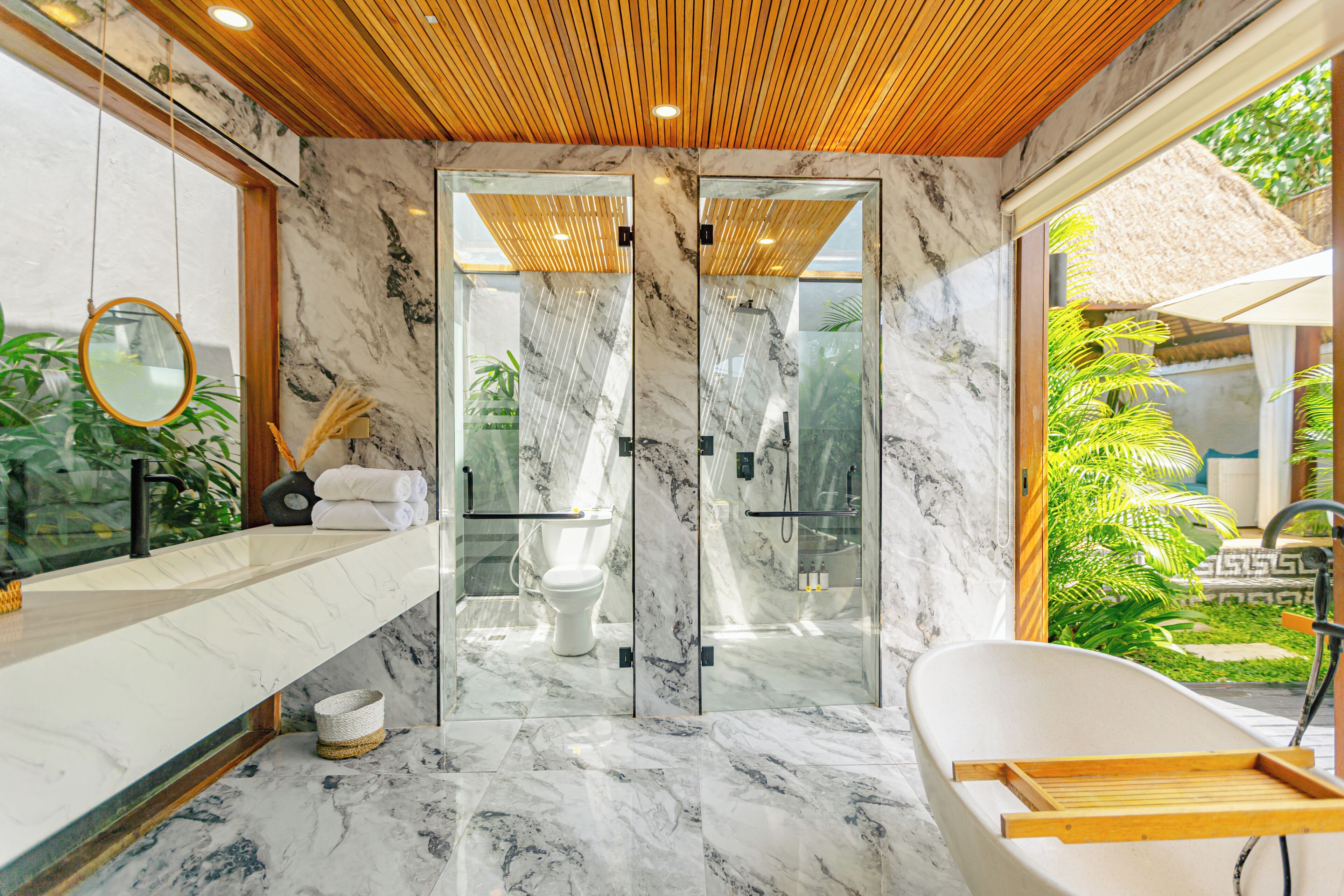 Un baño moderno con piso de mármol, techo de madera, ducha envuelta en vidrio, bañera independiente y un espejo grande.