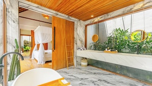 Un baño con bañera, zona de ducha y un espejo grande que refleja plantas.