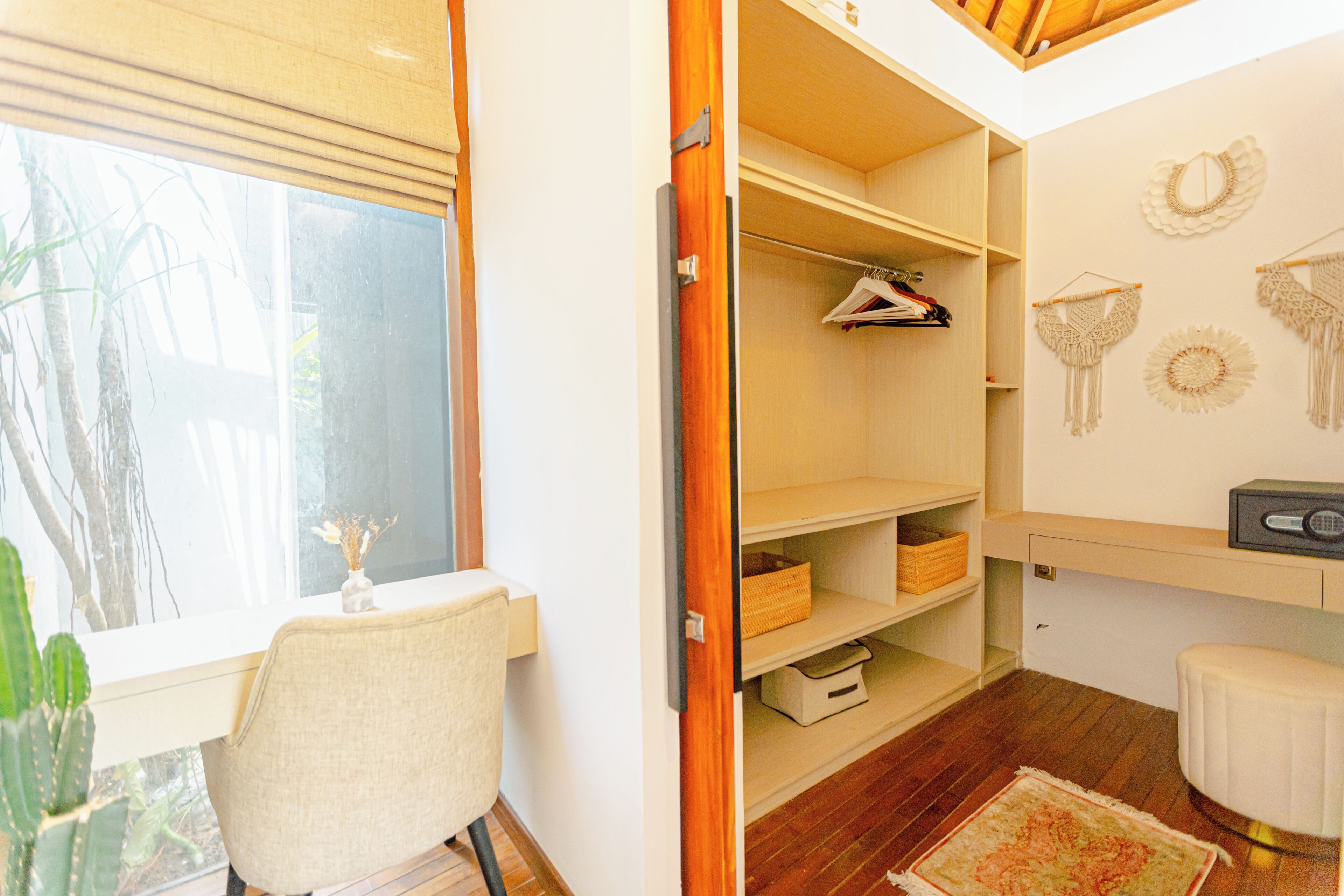 A room with a wooden floor, a chair, a desk, a window with a view of trees, a closet with shelves, and wall decorations.