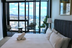 Ein Hotelzimmer mit einem großen Bett, Blick auf die Stadt durch raumhohe Fenster, einem kleinen runden Tisch und einem Stuhl.