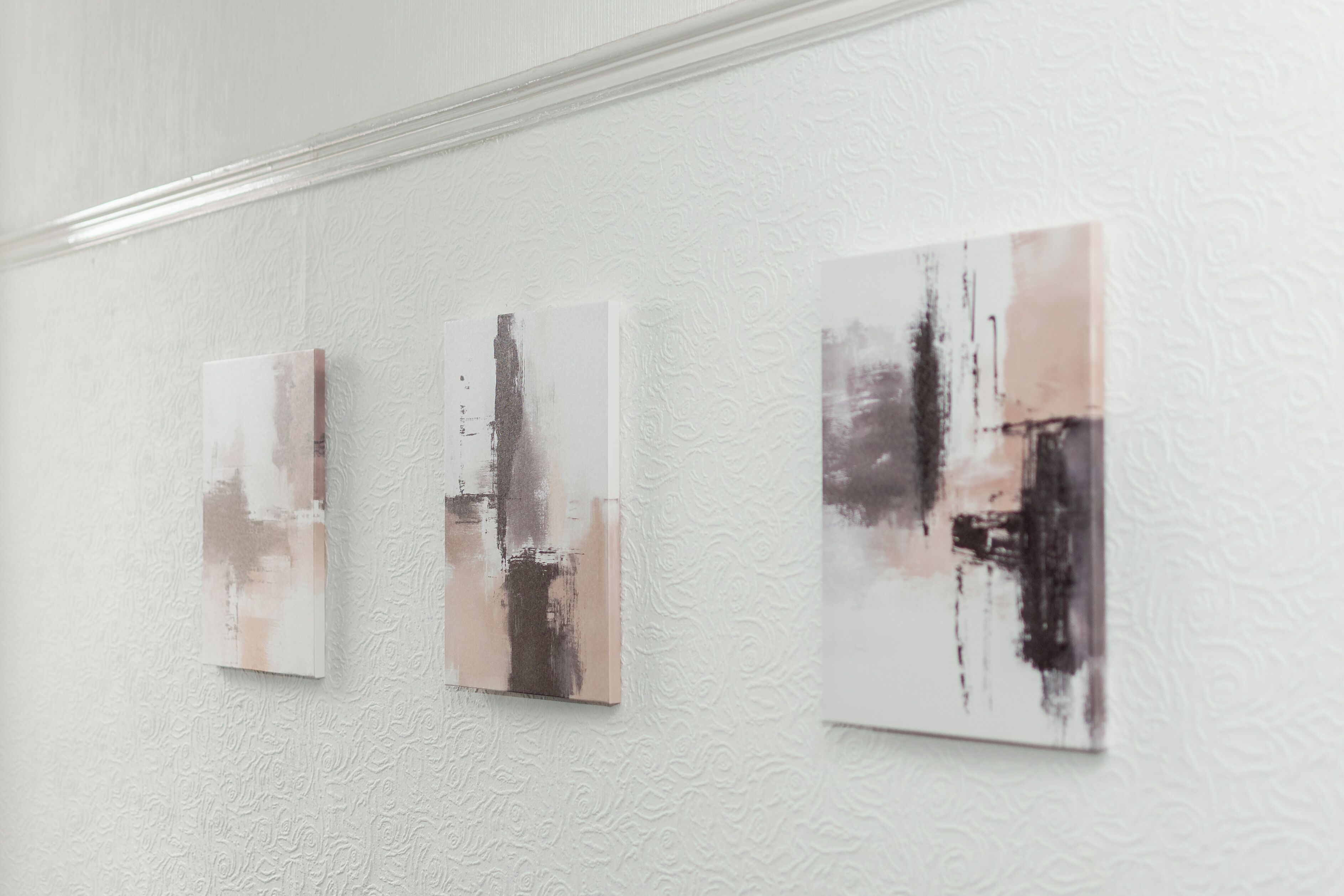 Three abstract paintings on a textured white wall.