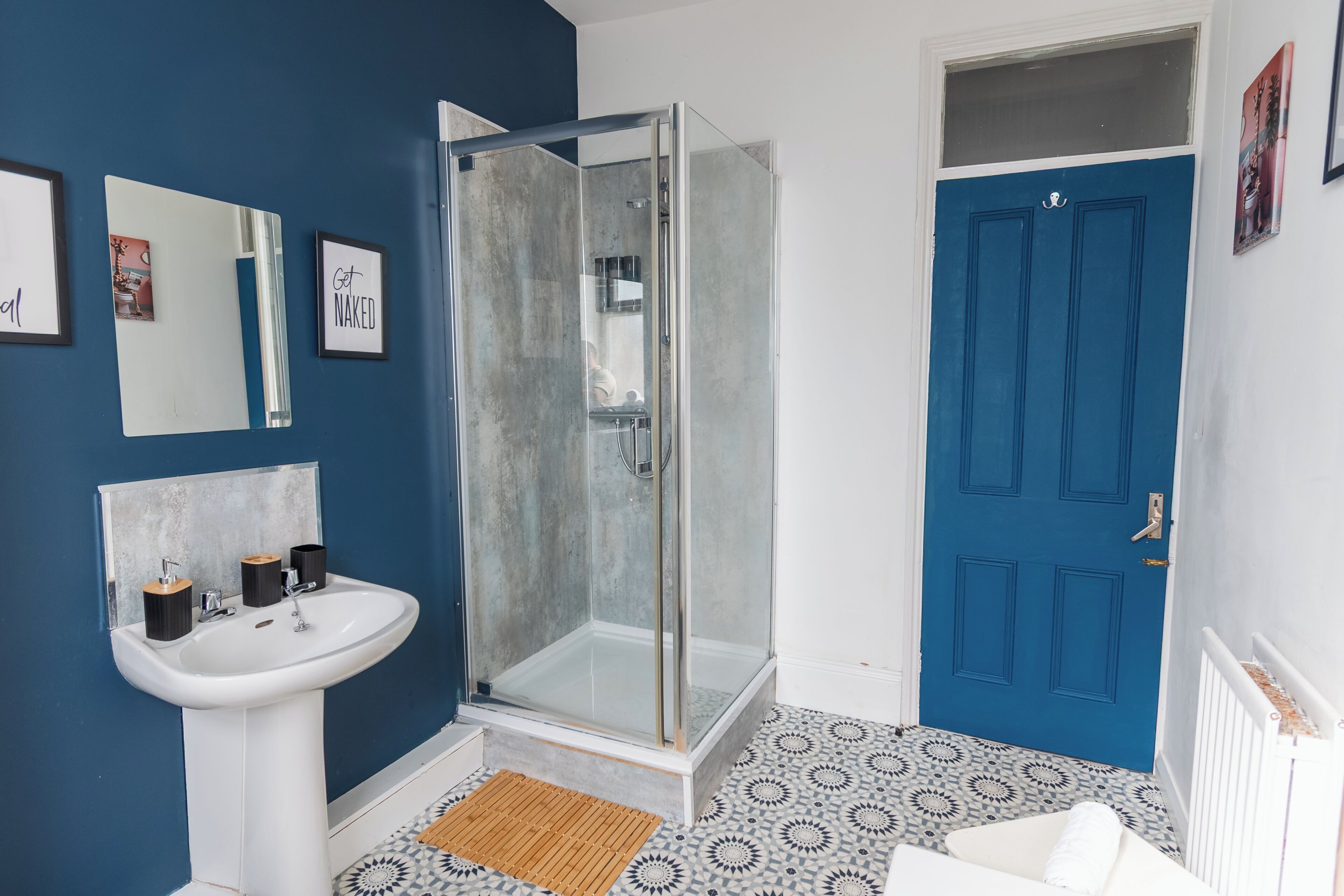 A bathroom with a white sink, a glass-enclosed shower, a blue door, and patterned floor tiles.