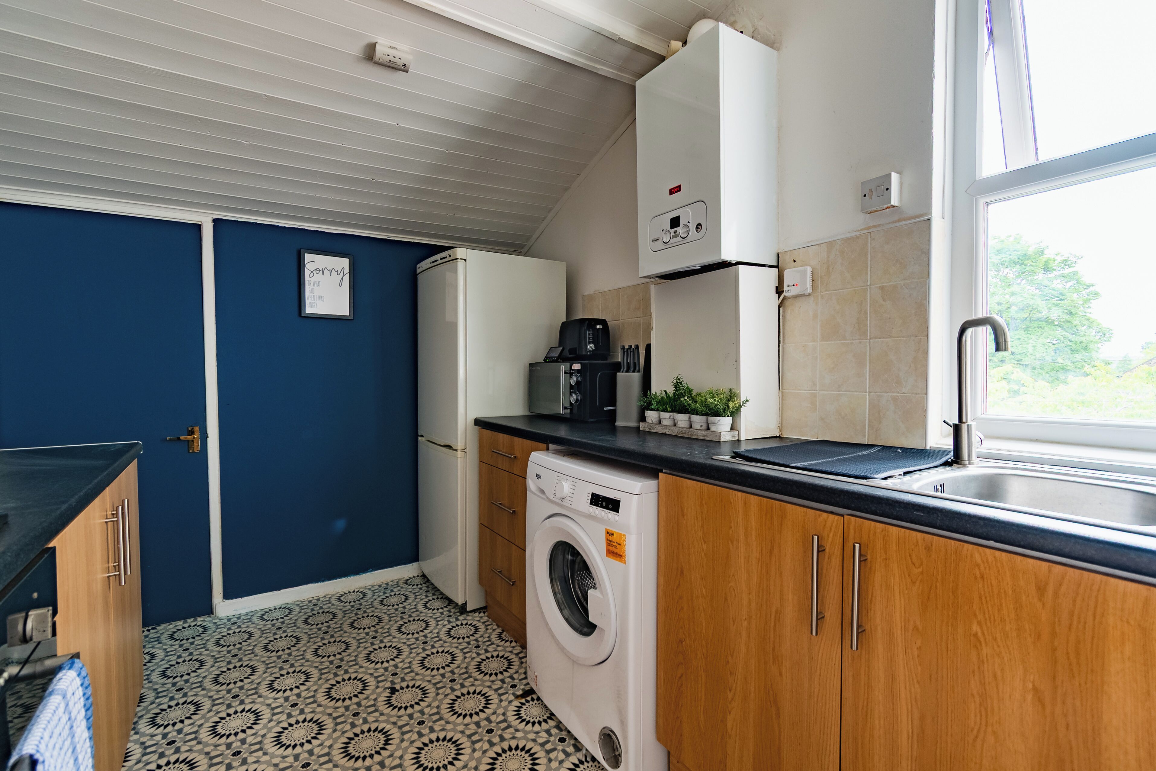 A compact kitchen with a washing machine, a coffee maker, and a window with a view.