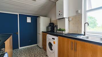 A compact kitchen with a washing machine, a coffee maker, and a window with a view.