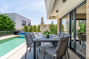 Ein Essbereich im Freien mit Pool, modernen Stühlen und einem Tisch für vier Personen.