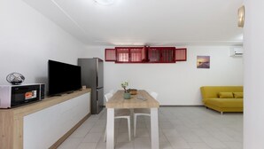 Un espacio habitable compacto con una mesa de comedor, sillas, un televisor, un refrigerador y un sofá.