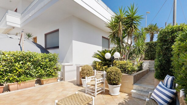 Un patio con una silla blanca, una mesita, plantas en macetas y una escalera que lleva a un edificio.