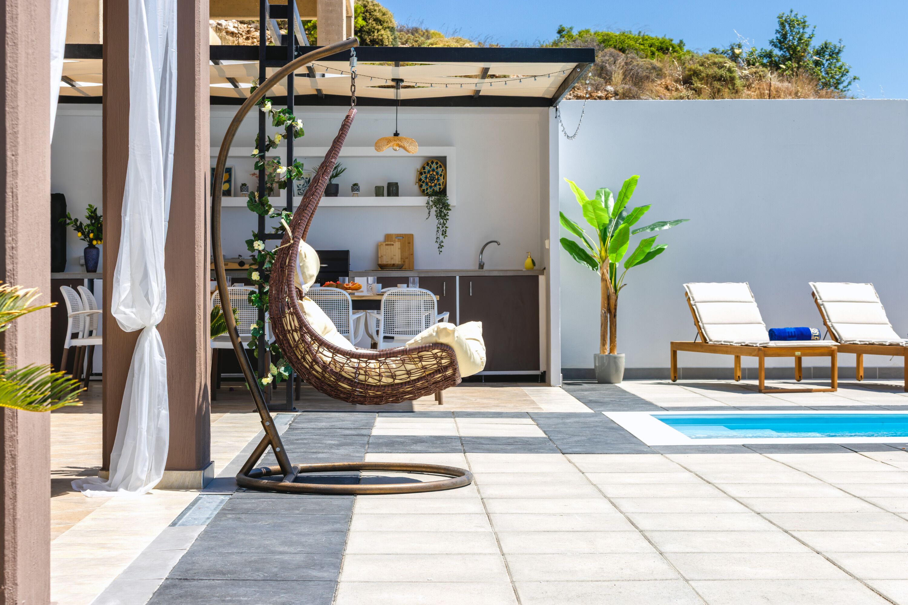 Un espace extérieur moderne comprenant un fauteuil suspendu, une piscine et un coin cuisine.
