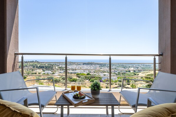 A balcony with two chairs, a table with a tray of food and drinks, and a potted plant.