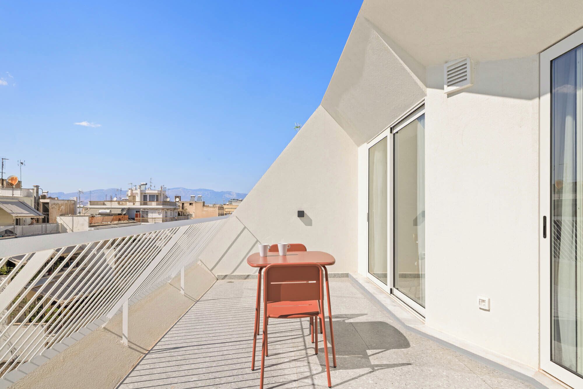Un balcón con mesa y sillas, un ventanal de vidrio y vistas a la ciudad.