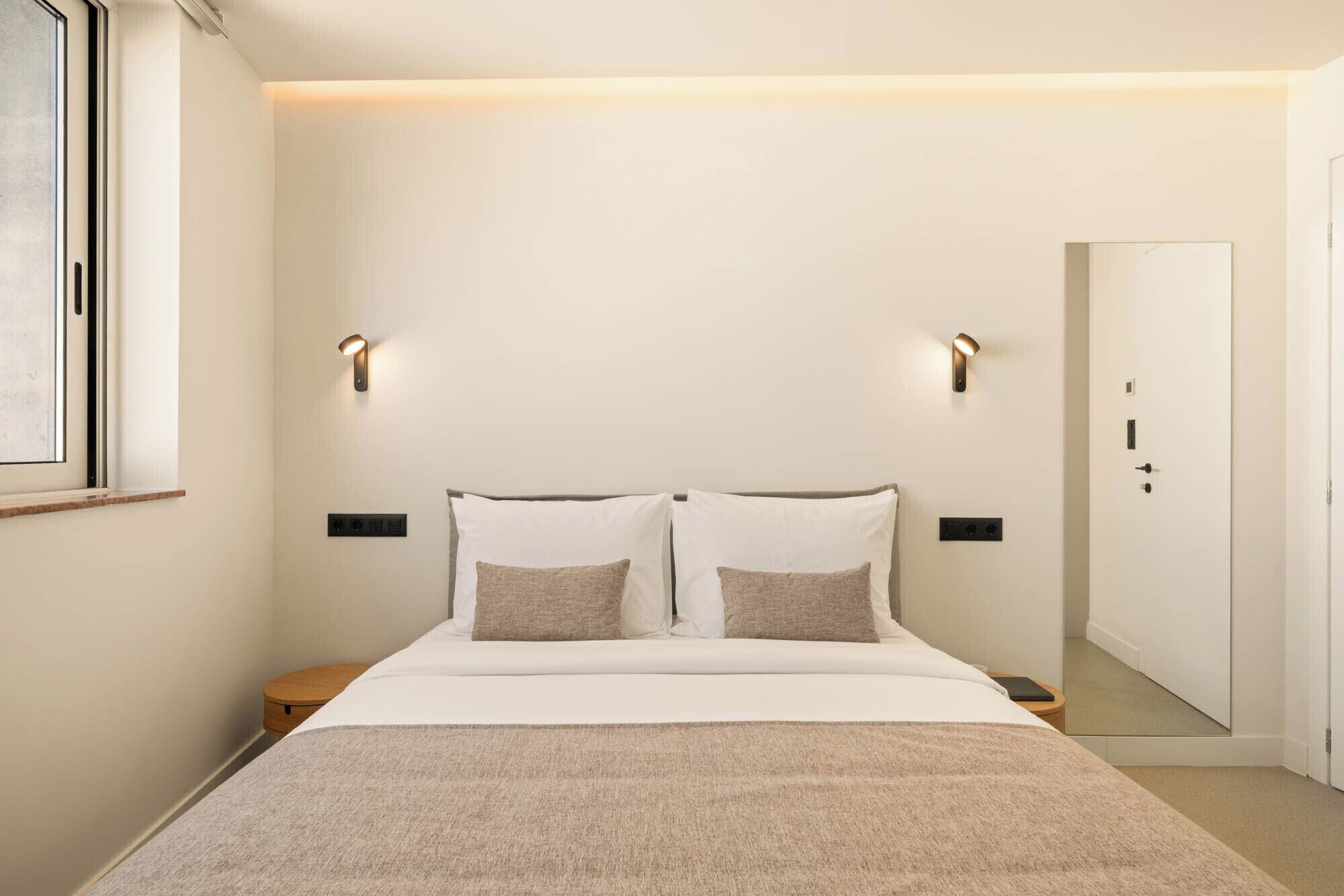 A hotel room with a bed, bedside tables, a nightstand, a mirror, and a door.