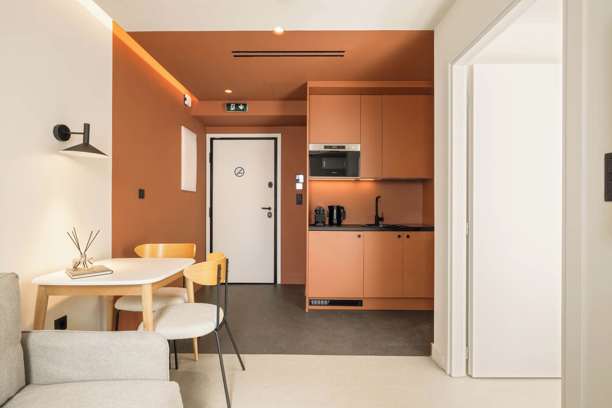 A compact hotel room with a kitchenette, a dining area with a table and chairs, and a sofa.