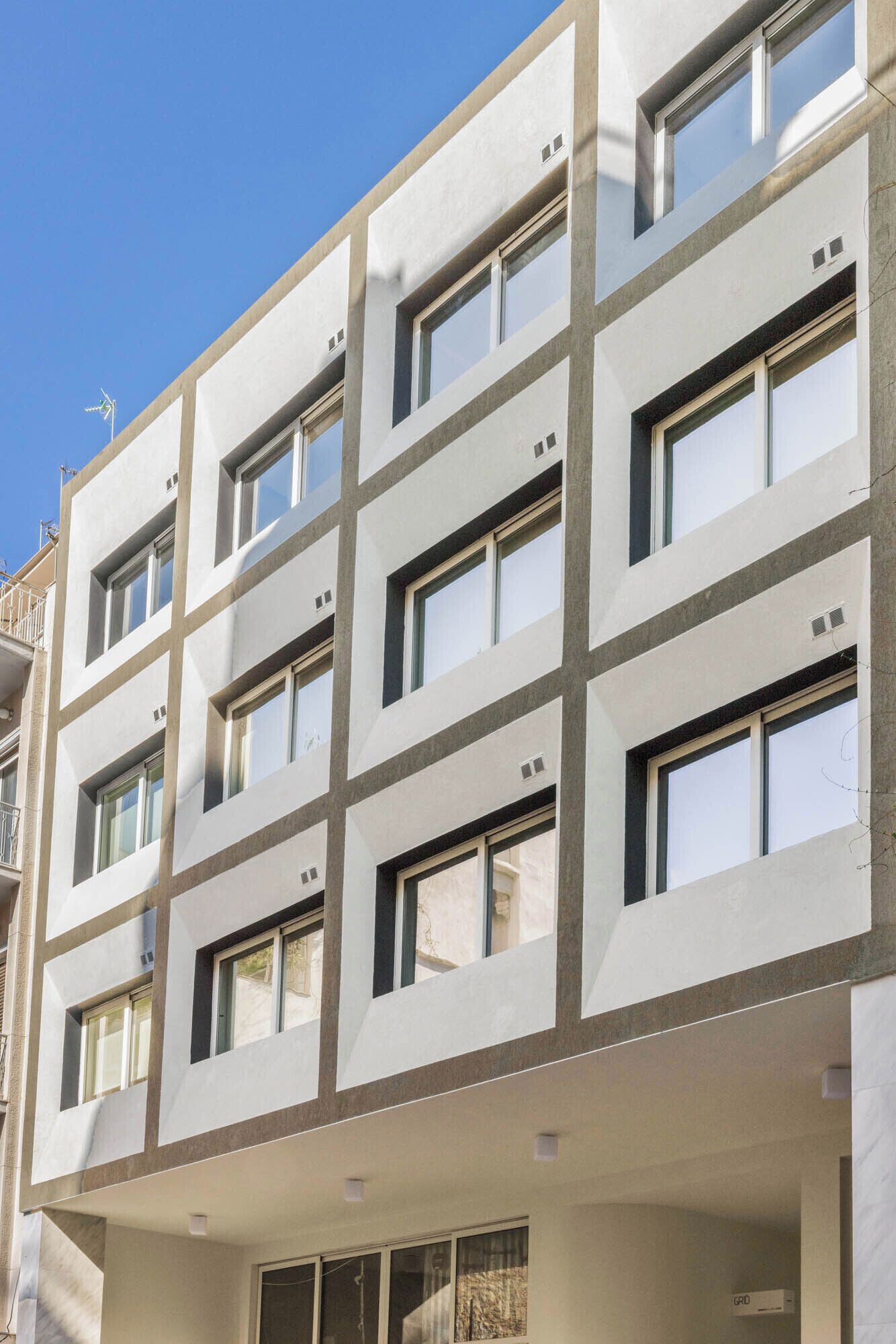 Un edificio de varios pisos con un estilo arquitectónico moderno, que presenta una fachada enrejada con ventanas y balcones uniformemente distribuidos.