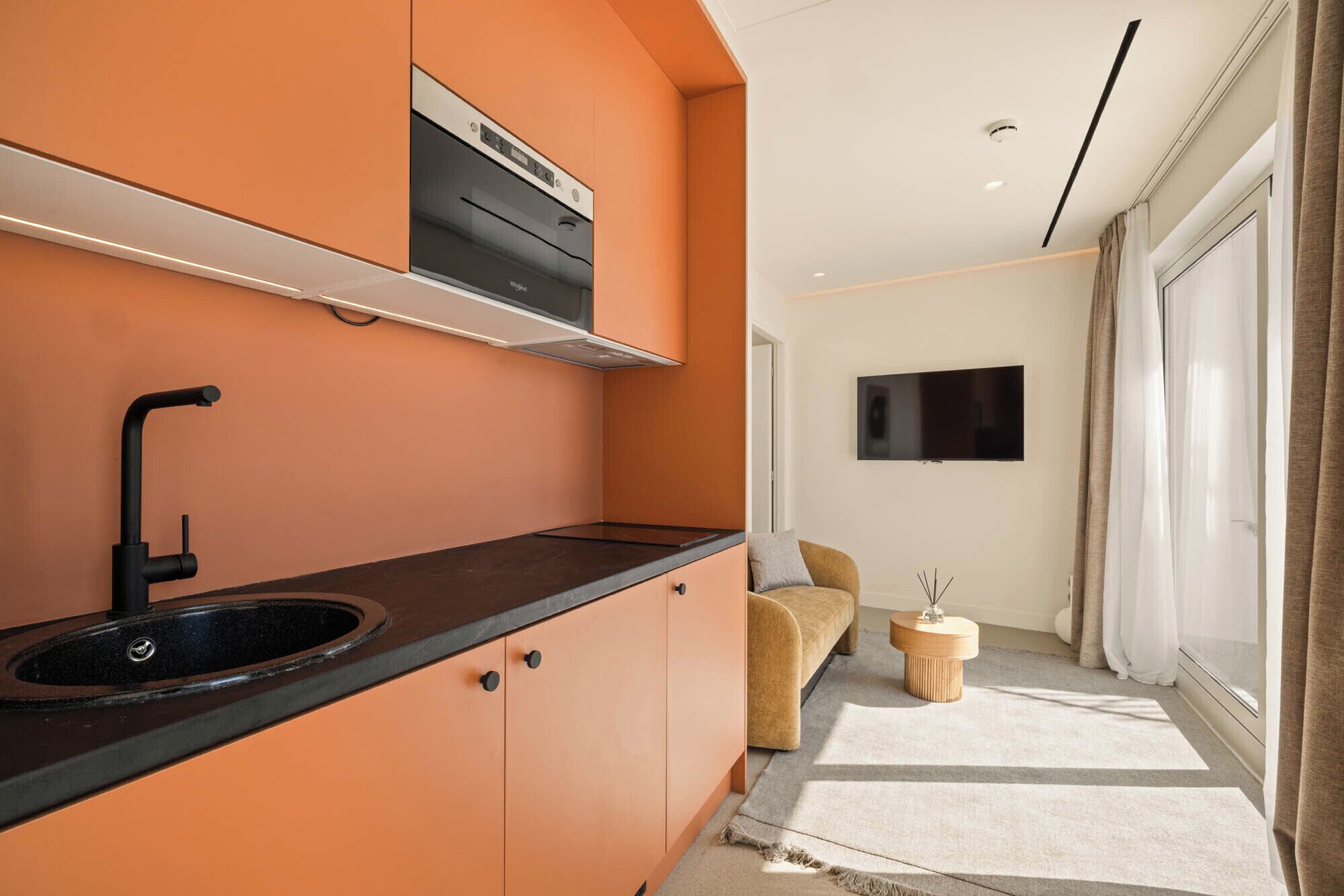 A modern kitchen with a black sink, orange cabinetry, and a built-in oven.
