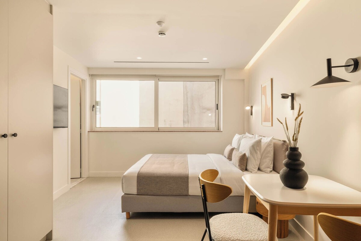 Quarto moderno com cama, mesa de cabeceira, cadeira e janela.