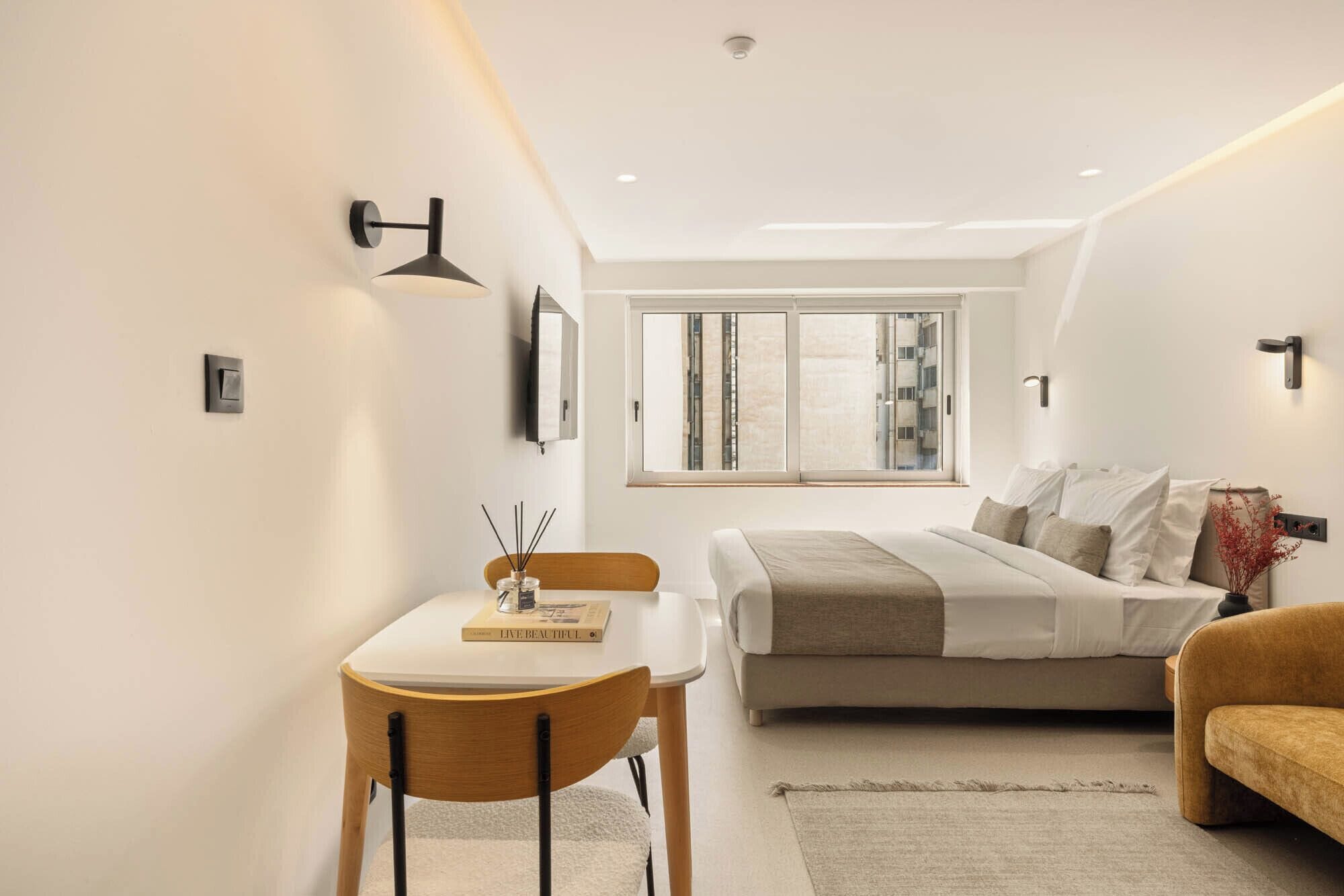 Camera moderna con un letto, un comodino, una sedia, una finestra e un punto luce a parete.
