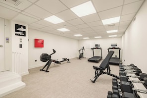 Academia com equipamentos de cardio, halteres e um armário vermelho para mangueira de incêndio.