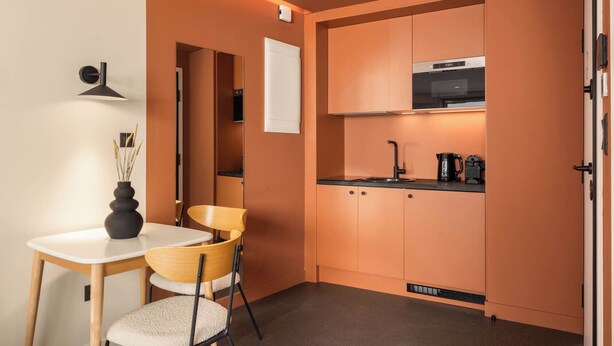 A compact kitchen with a single dining table and chairs, a built-in oven, and a coffee maker. - Grid II by Zoia Living (Athens)