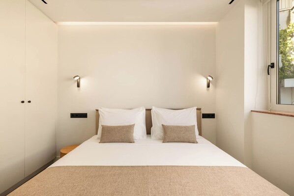 A bedroom with a bed, two bedside lamps, and a window. - Grid II by Zoia Living (Athens)