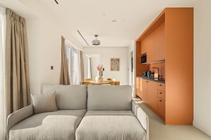 Een moderne woonkamer met een bank, een eethoek met een tafel en stoelen, en een keuken met kasten en apparatuur.