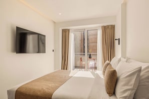 Hotelkamer met een bed, een flatscreen televisie aan de muur, een balkon met een tafel en stoelen, en een schuifglazen deur.