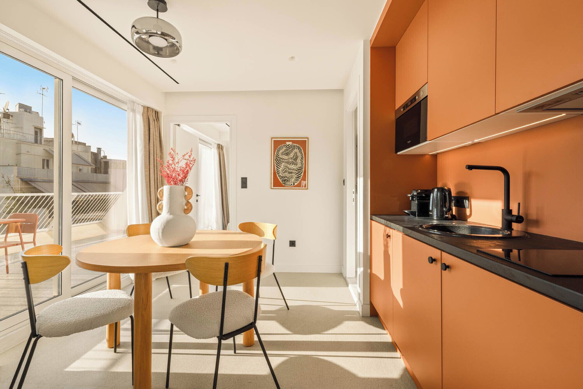 A modern kitchen with orange cabinetry, a black countertop, and a stainless steel range hood.